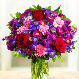 Bouquet of red roses, pink carnations, and purple daisies in a glass vase