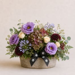 Mixed bouquet in a low stone container with purple, cream, and burgundy blooms