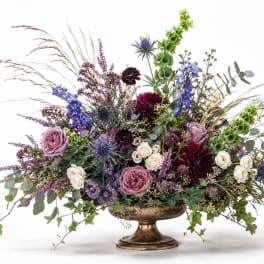 Mixed floral arrangement in a gold pedestal vase with purple, white, and green blooms