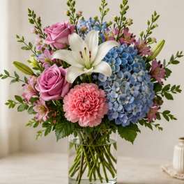Bouquet of pink roses, blue hydrangeas, white lily, and pink carnations in a glass vase
