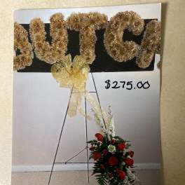 Gold tinsel letters on an easel with a red floral spray below