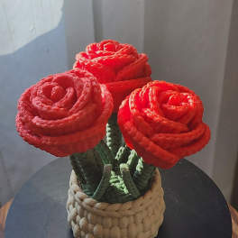 Three red rose-shaped flowers in a woven basket container