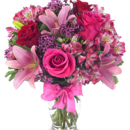Pink and red bouquet of roses and lilies in a glass vase with a ribbon