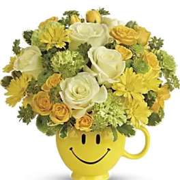 Yellow and white flower arrangement in a smiley-face mug