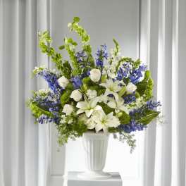 White lilies and roses arranged with blue flowers in a white vase.