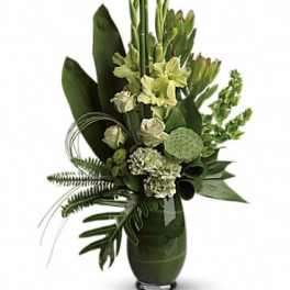 Tall green floral arrangement in a dark vase with tropical leaves and pale blooms