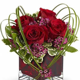 Red roses and purple filler flowers in a square glass vase