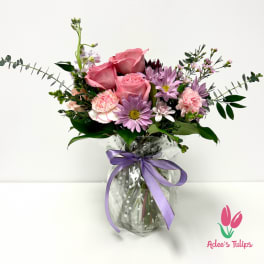 Pink roses and lavender daisies in a glass vase with a purple ribbon