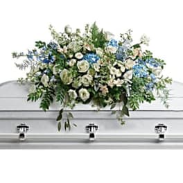 White casket spray with blue flowers and greenery