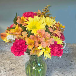 Mixed bouquet of yellow daisies, pink carnations, and peach alstroemeria in a glass vase