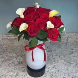 Bouquet of red roses and white calla lilies in a white vase with a red ribbon