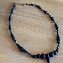 Black beaded necklace with a pointed pendant on a wooden surface