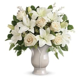 White lilies and cream roses arranged in a pale vase