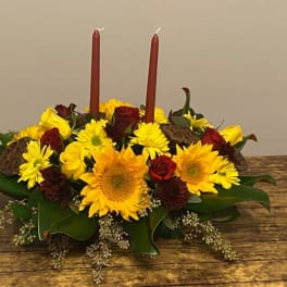 Low floral centerpiece with yellow sunflowers and red roses around two red candles