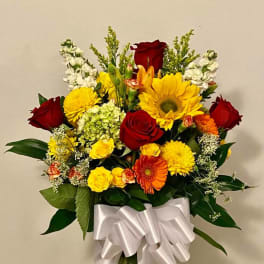 Mixed bouquet of red, yellow, and orange flowers in a glass vase with a white ribbon