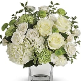White roses and green pompons arranged in a clear square vase