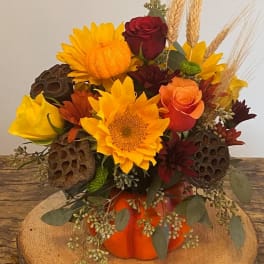 Autumn bouquet with sunflowers, roses, and wheat in an orange pumpkin vase