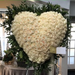 Heart-shaped arrangement of cream roses with dark greenery