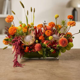 Low rectangular arrangement of orange and yellow flowers in a glass vase