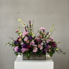 Mixed purple and pink flower arrangement in a wooden box