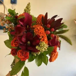 Handheld bouquet of red and orange flowers with green foliage
