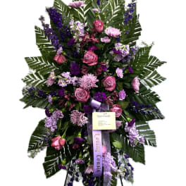 Standing floral spray with pink and purple flowers on a black easel