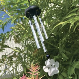Metal wind chime hanging among green foliage with a paw-shaped ornament