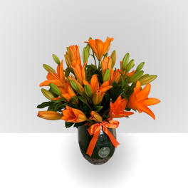 Orange lilies in a dark glass vase with an orange ribbon