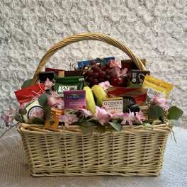 Gift basket with chocolates, fruit, and pink flowers in a wicker basket