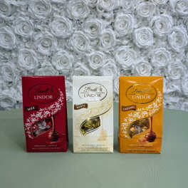 Three Lindt Lindor chocolate boxes on a table in front of a white rose wall.