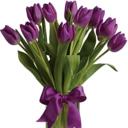 Purple tulips in a clear glass vase tied with a purple ribbon