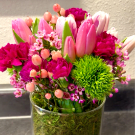 Pink tulips and magenta flowers arranged in a clear glass vase
