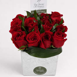 Red roses arranged in a square silver container with a card pick
