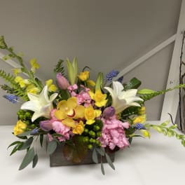 Mixed bouquet with white lilies, yellow orchids, and pink carnations in a wooden container