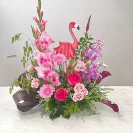 Pink floral arrangement with roses, orchids, and a flamingo decoration