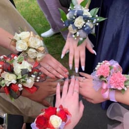 Hands wearing floral wrist corsages with roses and ribbons