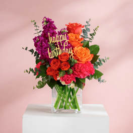 Bouquet of orange and magenta flowers in a clear glass vase with a happy birthday sign