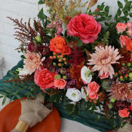 Colorful bouquet with roses, daisies, and mixed blooms beside orange plates