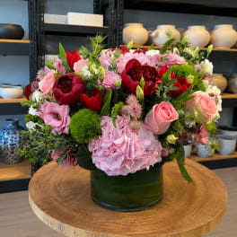 Mixed pink and red flower arrangement in a green glass vase