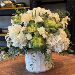 White floral arrangement in a white hatbox with trailing greenery