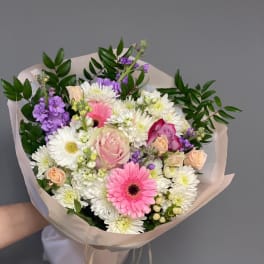 Hand-tied bouquet of pink, white, and purple flowers wrapped in pale paper