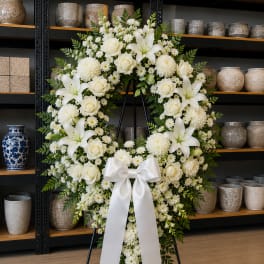 White floral standing wreath on an easel with a satin bow