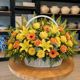 Basket arrangement of yellow lilies, roses, and orange gerbera daisies