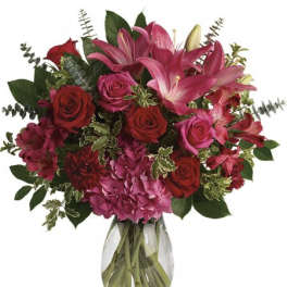 Arrangement of red and pink roses, lilies, carnations, and hydrangeas in a clear glass vase