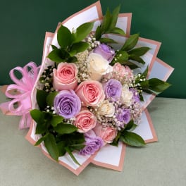 Bouquet of pink, lavender, and white roses with baby’s breath and ribbon wrap