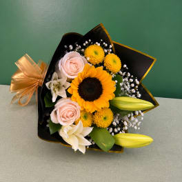 Bouquet of sunflowers, pale pink roses, and white lilies wrapped in black paper