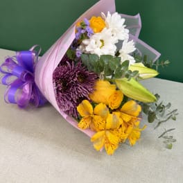 Bouquet of yellow, white, and purple flowers wrapped in pink paper
