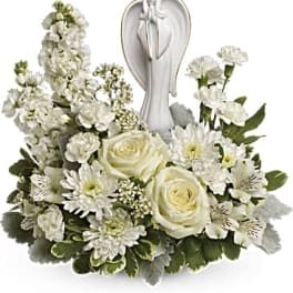 White floral arrangement with roses and daisies around an angel figurine