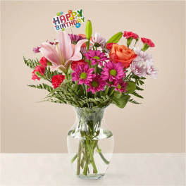 Mixed bouquet in a clear glass vase with a birthday sign