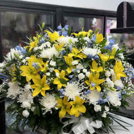 Large bouquet of yellow lilies, white chrysanthemums, and blue accents with a white ribbon
